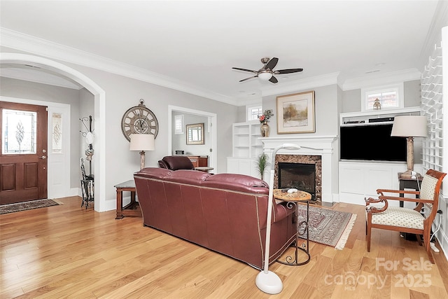 living area featuring light wood finished floors, plenty of natural light, a fireplace, and ornamental molding