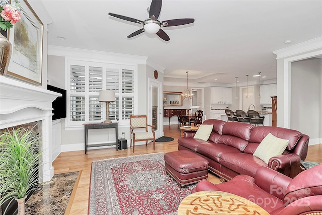 living room with crown molding, ceiling fan with notable chandelier, and light hardwood / wood-style flooring