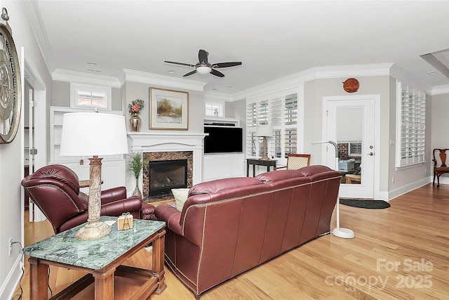 living room featuring crown molding, light wood finished floors, a high end fireplace, ceiling fan, and baseboards