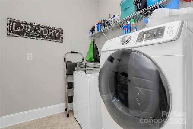 clothes washing area with laundry area, washing machine and dryer, and baseboards