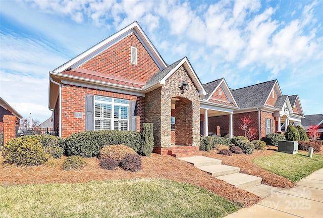 view of front of home featuring metal roof, stone siding, brick siding, and a standing seam roof