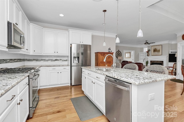 kitchen with white cabinetry, hanging light fixtures, stainless steel appliances, light stone countertops, and a kitchen island with sink