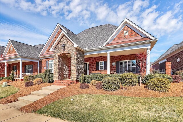 craftsman-style house featuring a shingled roof, stone siding, and brick siding