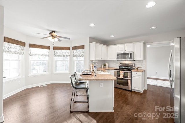 kitchen with ceiling fan, backsplash, a breakfast bar area, white cabinets, and appliances with stainless steel finishes