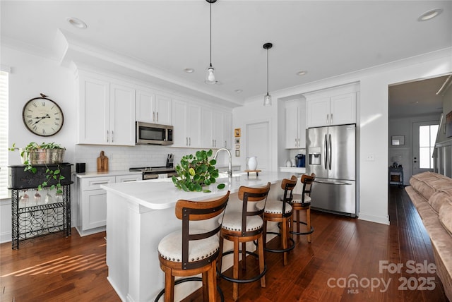 kitchen featuring stainless steel appliances, crown molding, a center island with sink, white cabinetry, and hanging light fixtures