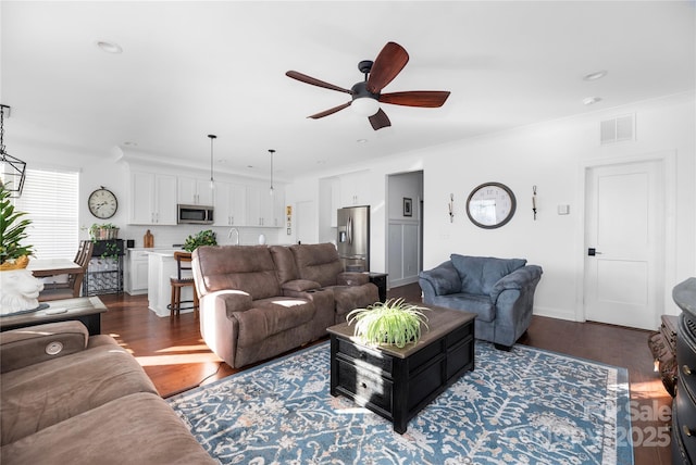 living room with ceiling fan, crown molding, and dark wood-type flooring