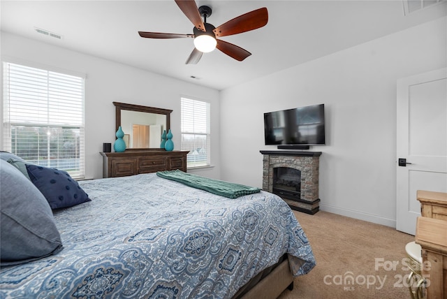 bedroom with multiple windows, light colored carpet, ceiling fan, and a fireplace