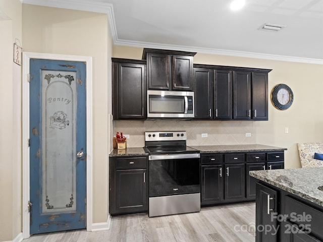 kitchen with light wood finished floors, tasteful backsplash, dark stone counters, stainless steel appliances, and crown molding