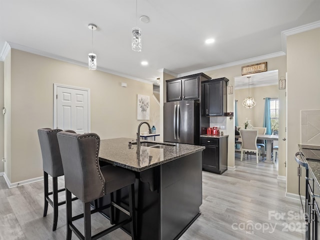 kitchen featuring a breakfast bar area, dark stone counters, a sink, and freestanding refrigerator