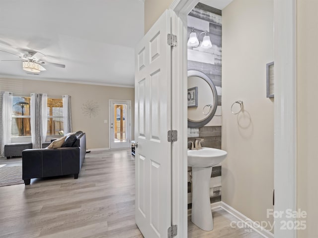 bathroom with a ceiling fan, ornamental molding, a sink, wood finished floors, and baseboards