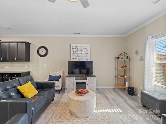 living area with a ceiling fan, visible vents, baseboards, ornamental molding, and light wood-type flooring