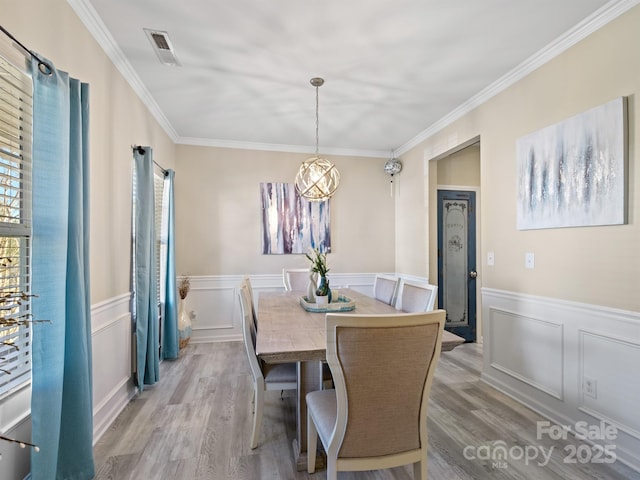 dining area featuring visible vents, a wainscoted wall, crown molding, light wood-type flooring, and a decorative wall