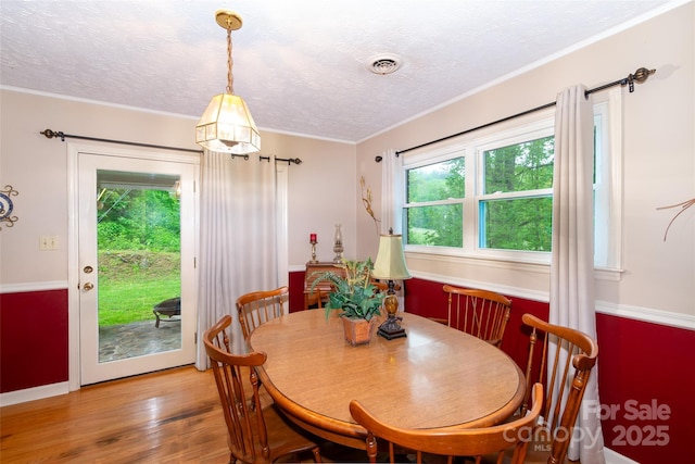 dining space featuring light wood-type flooring, visible vents, a textured ceiling, and ornamental molding