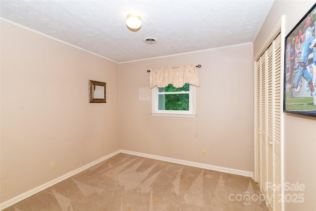 carpeted empty room featuring visible vents, crown molding, a textured ceiling, and baseboards