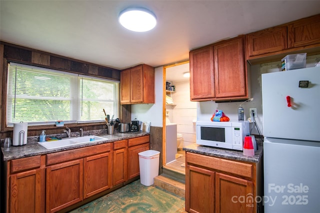 kitchen featuring dark countertops, white appliances, brown cabinets, and a sink