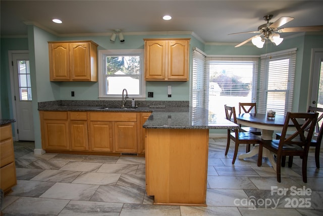 kitchen featuring sink, crown molding, a kitchen island, ceiling fan, and dark stone counters