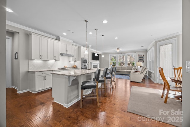 kitchen with a kitchen breakfast bar, light stone counters, pendant lighting, a center island with sink, and white cabinets