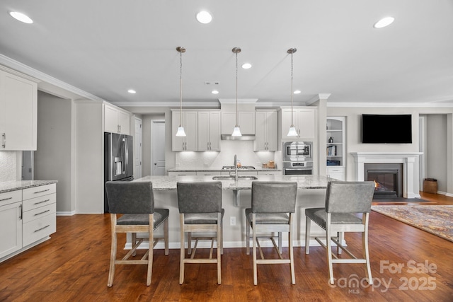 kitchen featuring light stone countertops, decorative light fixtures, crown molding, and an island with sink