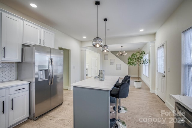 kitchen with stainless steel refrigerator with ice dispenser, backsplash, white cabinets, a kitchen island, and hanging light fixtures