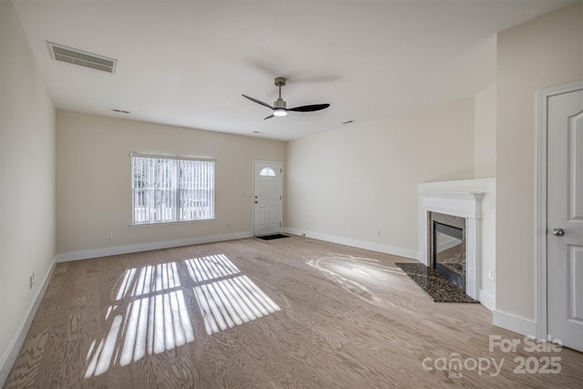 unfurnished living room featuring a high end fireplace, light hardwood / wood-style flooring, and ceiling fan