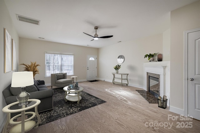 living room with a high end fireplace, light hardwood / wood-style floors, and ceiling fan