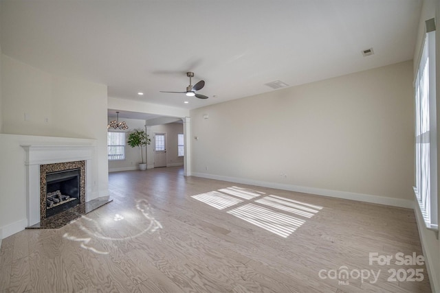 unfurnished living room with a premium fireplace, light hardwood / wood-style flooring, and ceiling fan with notable chandelier