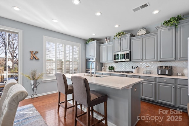 kitchen featuring tasteful backsplash, stainless steel appliances, sink, gray cabinets, and an island with sink