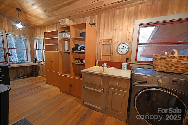 washroom featuring cabinets, sink, light hardwood / wood-style flooring, washer / dryer, and wood walls