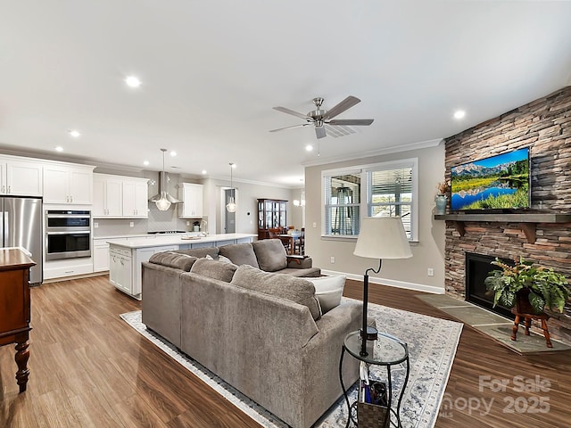 living room with ceiling fan, light wood-type flooring, a stone fireplace, and crown molding