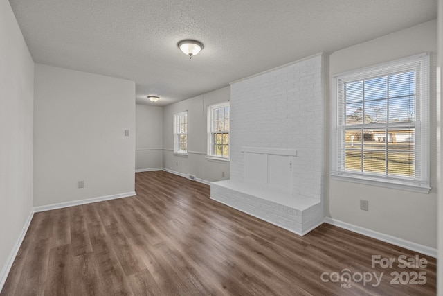 spare room with dark hardwood / wood-style floors, a textured ceiling, and a brick fireplace