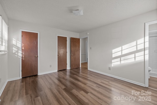 unfurnished bedroom with ensuite bathroom, a closet, a textured ceiling, and hardwood / wood-style flooring