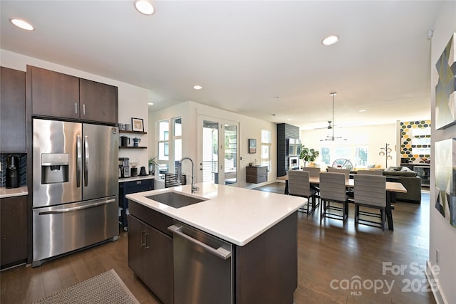 kitchen featuring sink, stainless steel appliances, dark brown cabinetry, a center island with sink, and decorative light fixtures