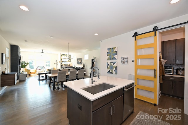 kitchen with sink, dark brown cabinets, dark hardwood / wood-style floors, a center island with sink, and a barn door