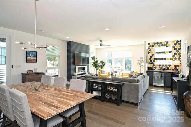 dining room with wine cooler, dark wood-type flooring, an inviting chandelier, bar area, and a large fireplace