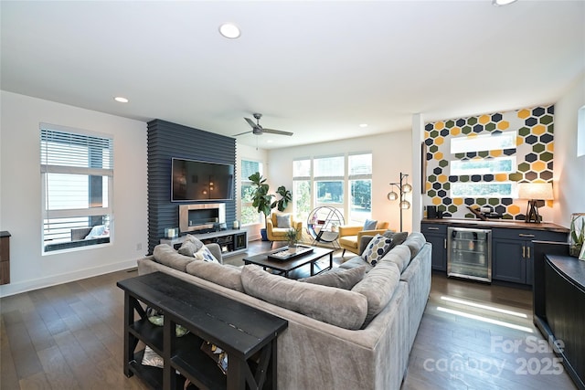 living room with dark wood-type flooring, ceiling fan, a large fireplace, bar area, and beverage cooler