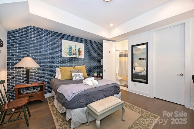 bedroom with dark hardwood / wood-style flooring, lofted ceiling, and ensuite bathroom