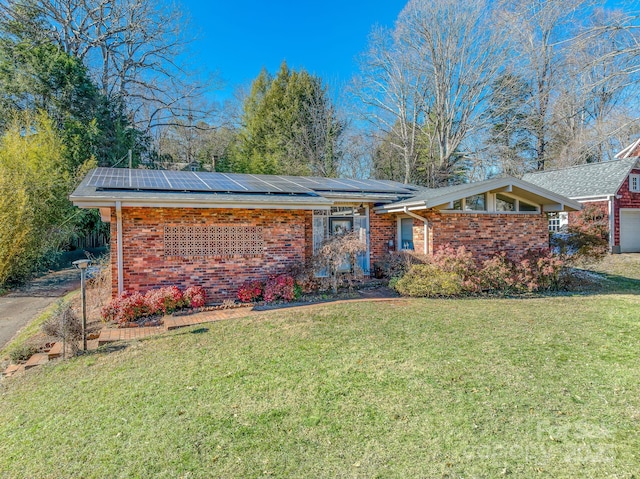 ranch-style home with a garage, a front yard, and solar panels