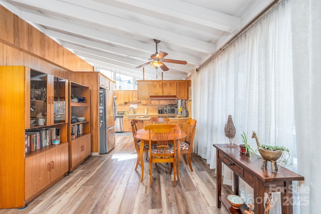 dining area featuring ceiling fan, wood walls, light hardwood / wood-style floors, lofted ceiling with beams, and sink