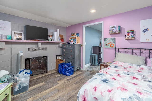 bedroom with a tiled fireplace and wood-type flooring