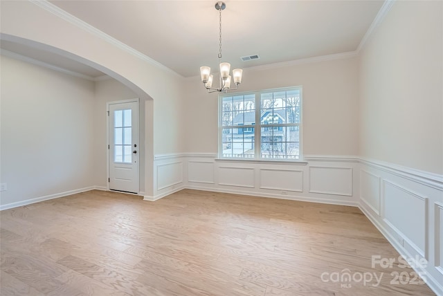 empty room with crown molding, an inviting chandelier, and light wood-type flooring