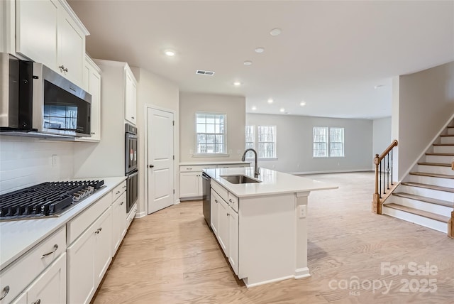 kitchen featuring white cabinetry, sink, light wood-type flooring, stainless steel appliances, and a center island with sink