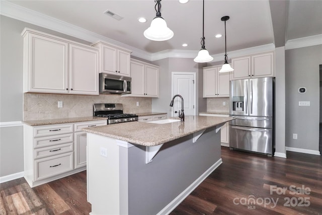 kitchen featuring light stone counters, stainless steel appliances, a kitchen island with sink, sink, and hanging light fixtures