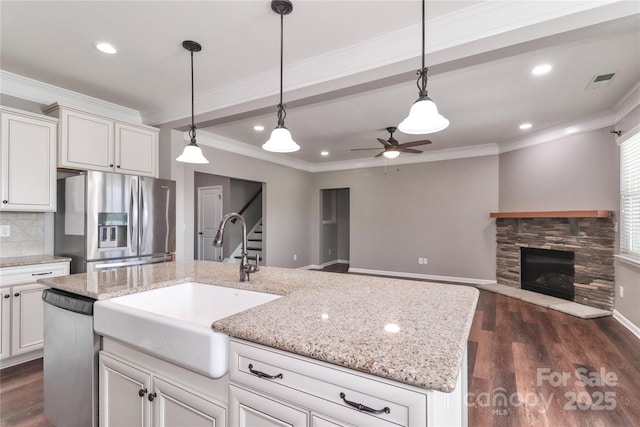 kitchen with ceiling fan, sink, a kitchen island with sink, a fireplace, and appliances with stainless steel finishes