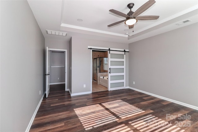 unfurnished bedroom with ensuite bathroom, ceiling fan, a barn door, dark hardwood / wood-style floors, and a tray ceiling