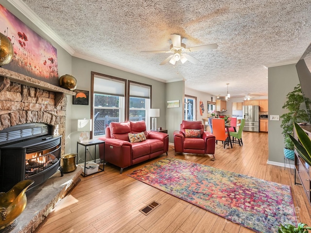 living room featuring a wood stove, ceiling fan, a healthy amount of sunlight, and ornamental molding