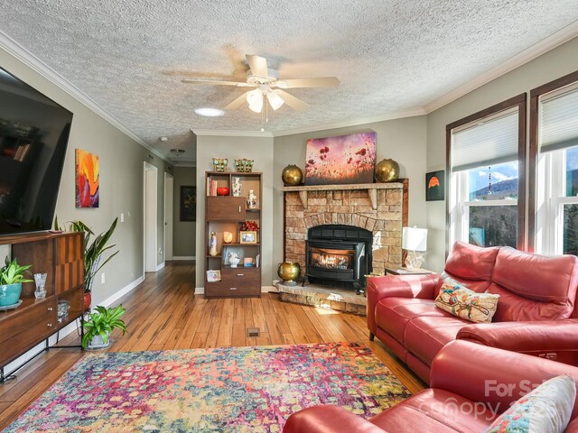 living room with a wood stove, ceiling fan, light hardwood / wood-style floors, a textured ceiling, and ornamental molding