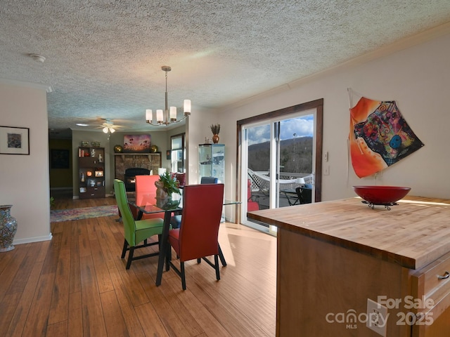 dining area with a textured ceiling, crown molding, wood-type flooring, and a fireplace