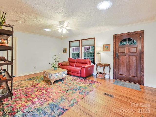 living room featuring ceiling fan, crown molding, hardwood / wood-style floors, and a textured ceiling