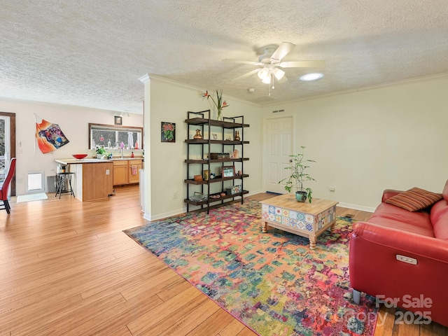 living room featuring ceiling fan, crown molding, a textured ceiling, and light hardwood / wood-style flooring