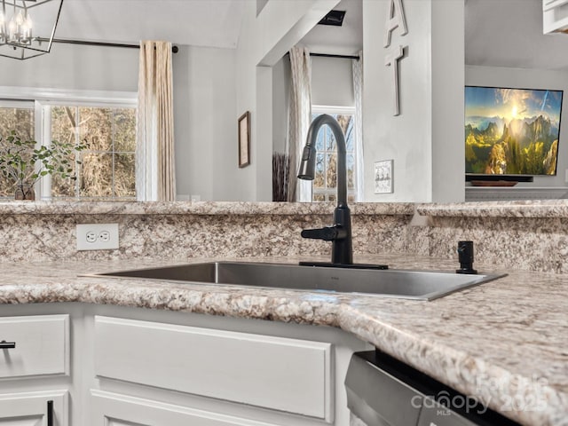 interior details with sink, stainless steel dishwasher, light stone counters, and a chandelier